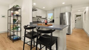 A modern kitchen with white cabinets, a stainless steel refrigerator, and a bar area with two black barstools. - Charming 3-bedroom Craftsman with AC + EV-Charger + very walkable in Ballard (Seattle)