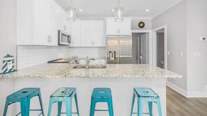 Una cocina moderna con armarios blancos, encimera de granito y tres taburetes turquesa.