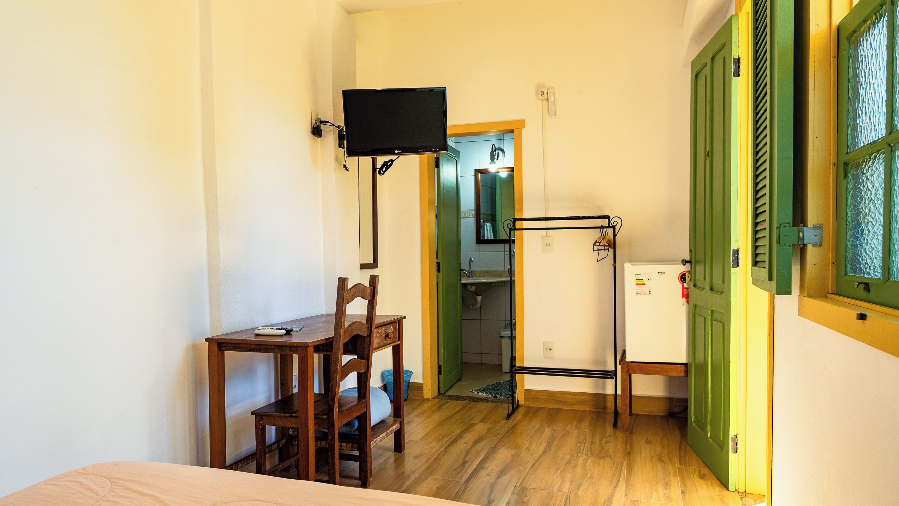 A room with a bed, a desk with a chair, a television, a refrigerator, and a green door.
