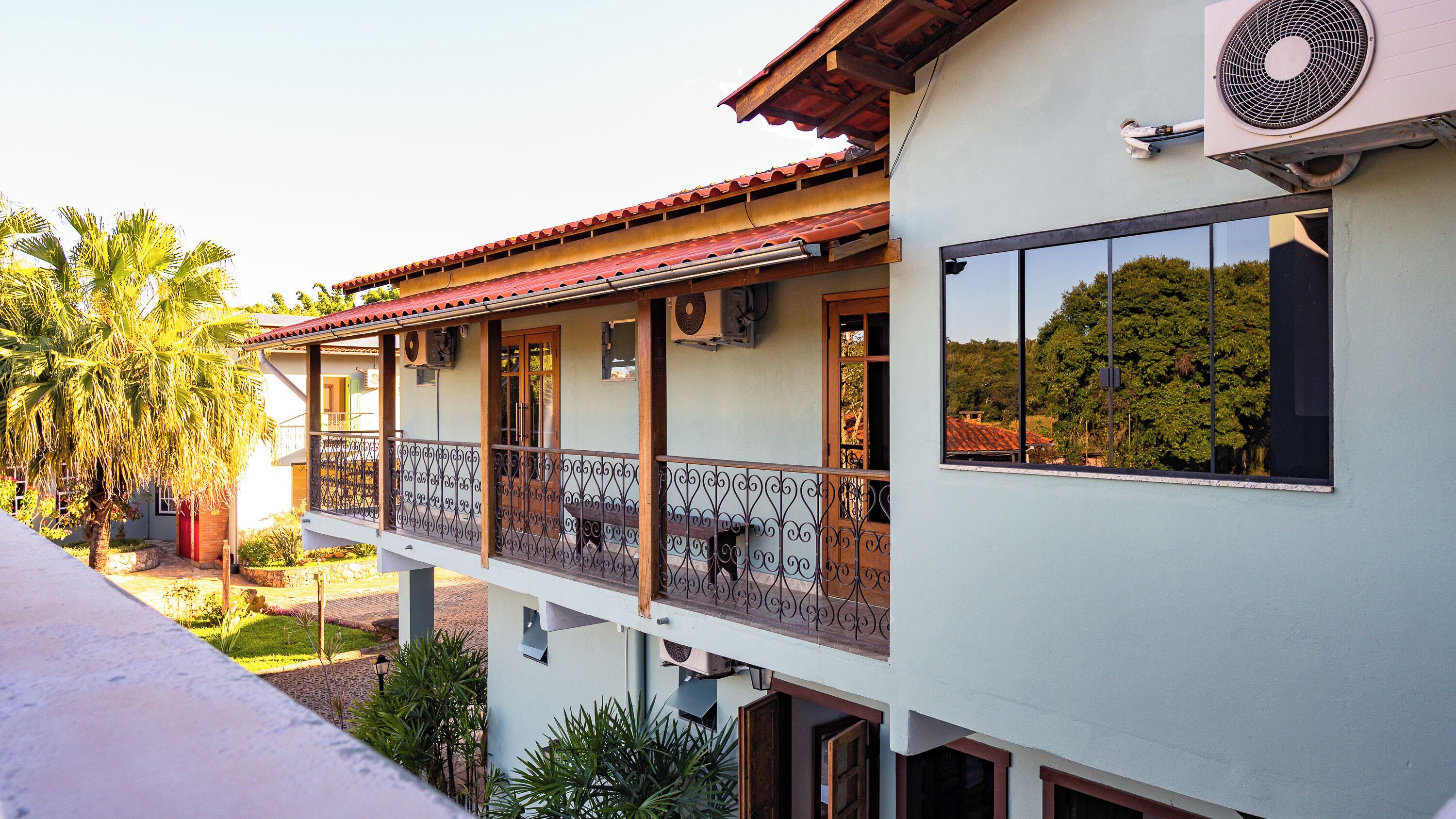 A two-story building with a balcony, a red-tiled roof, and an air conditioning unit.
