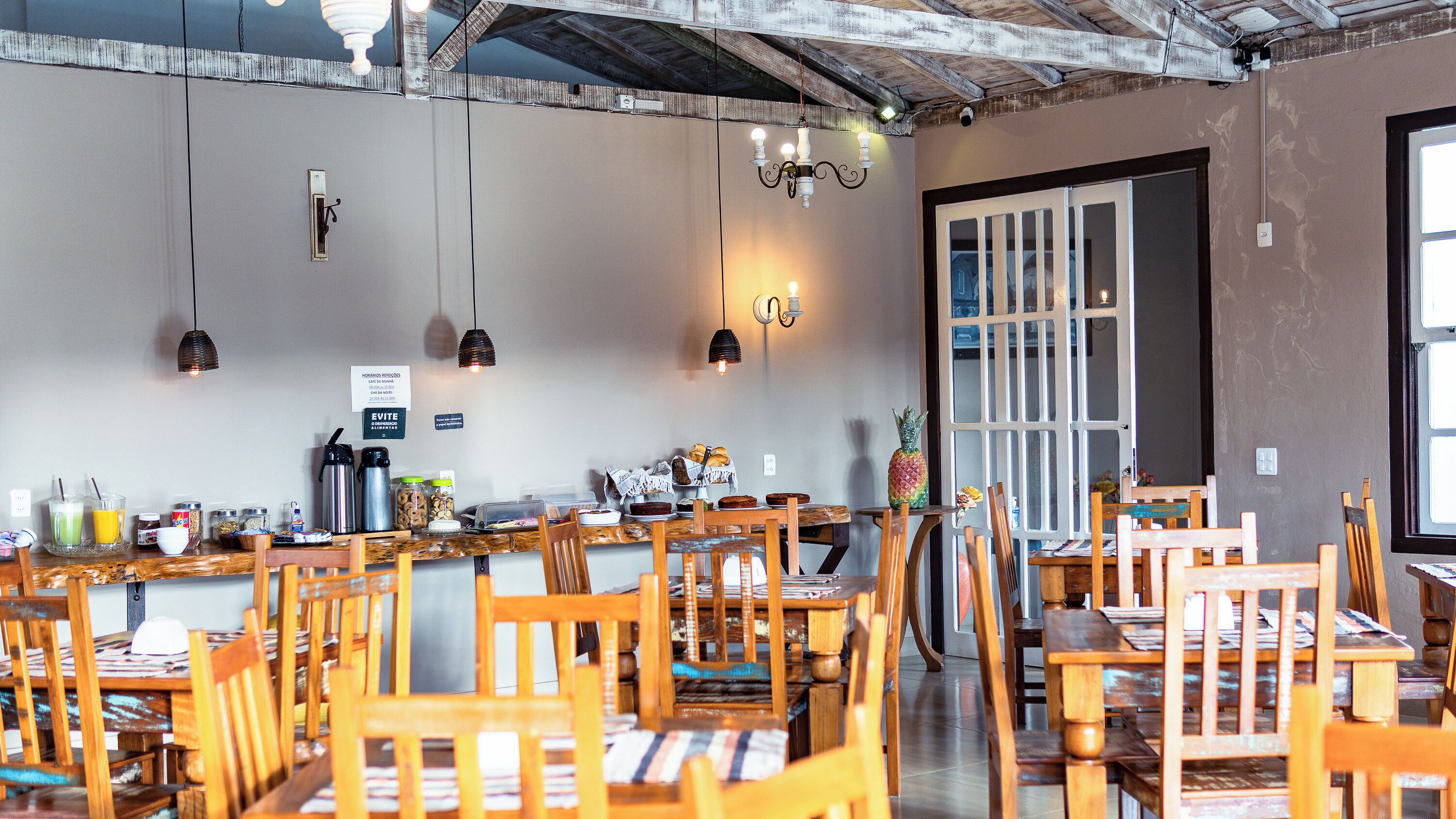 A restaurant with wooden tables and chairs, a bar area with drinks and snacks, and a view through a door.