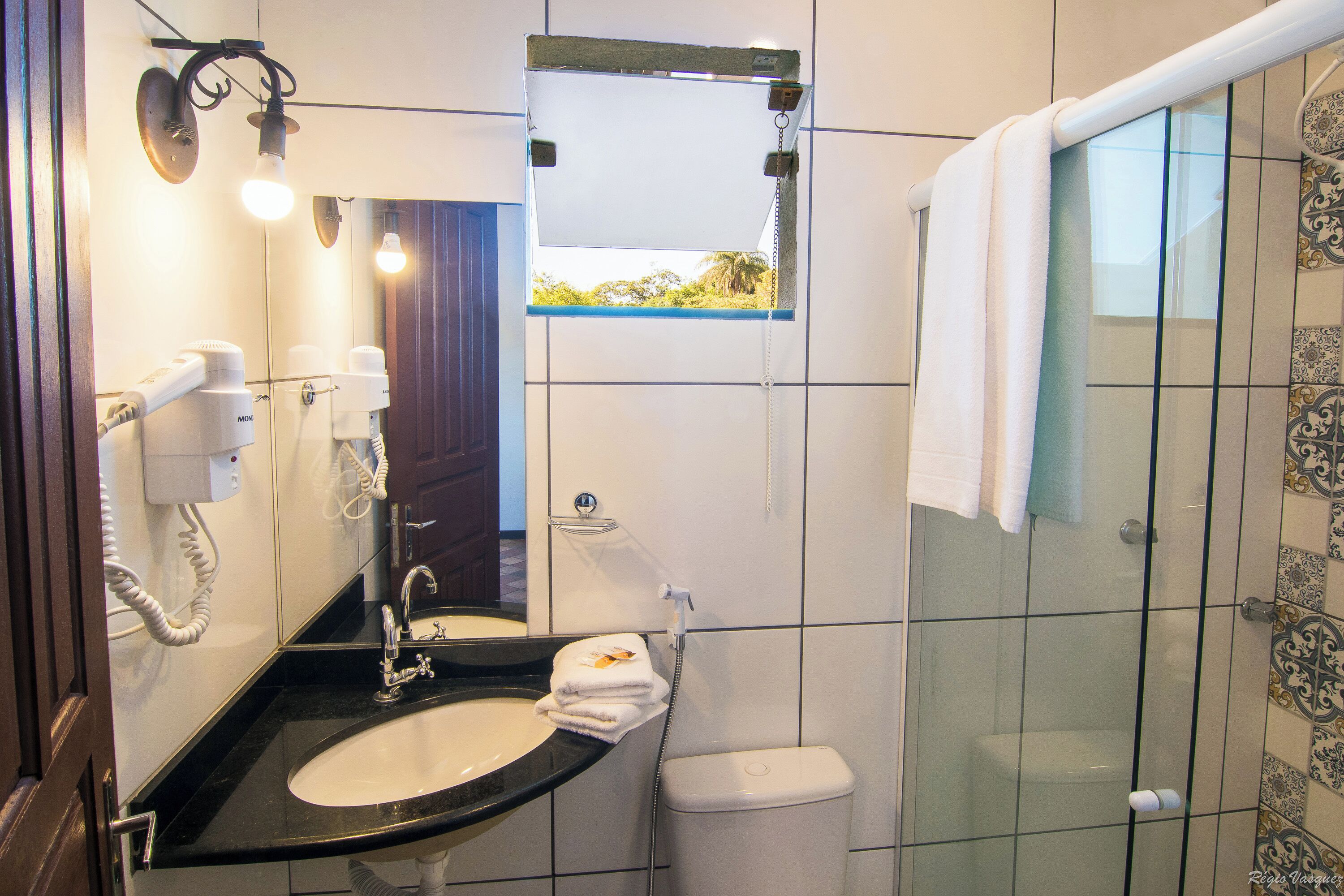 Baño con lavamanos, espejo, toallero y cabina de ducha.