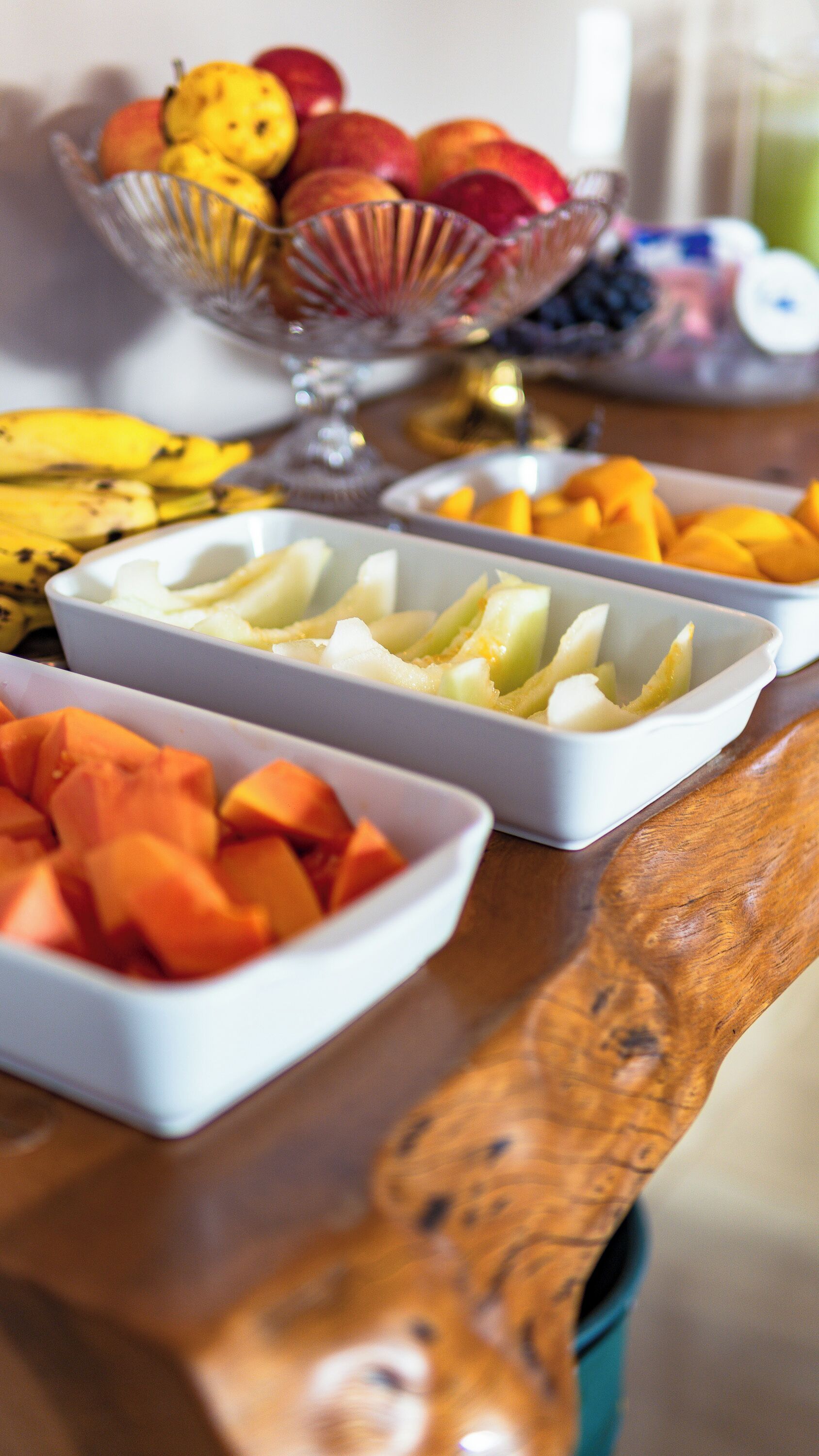 A table with various fruits in bowls, including apples, bananas, and oranges.