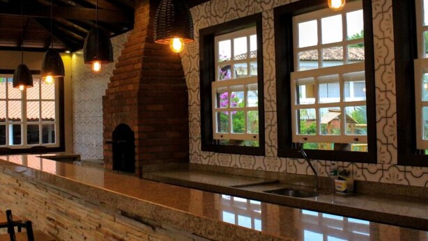 A restaurant with a stone wall, wooden ceiling, and hanging pendant lights. - Pousada da Sirlei (Tiradentes)