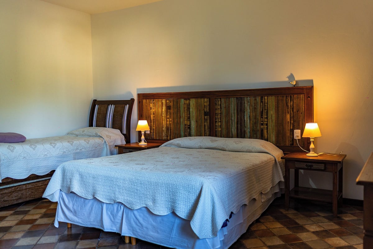 Ein Hotelzimmer mit zwei Betten, einem Holzkopfstück, Nachttischlampen, einem kleinen Tisch und einem gefliesten Boden.