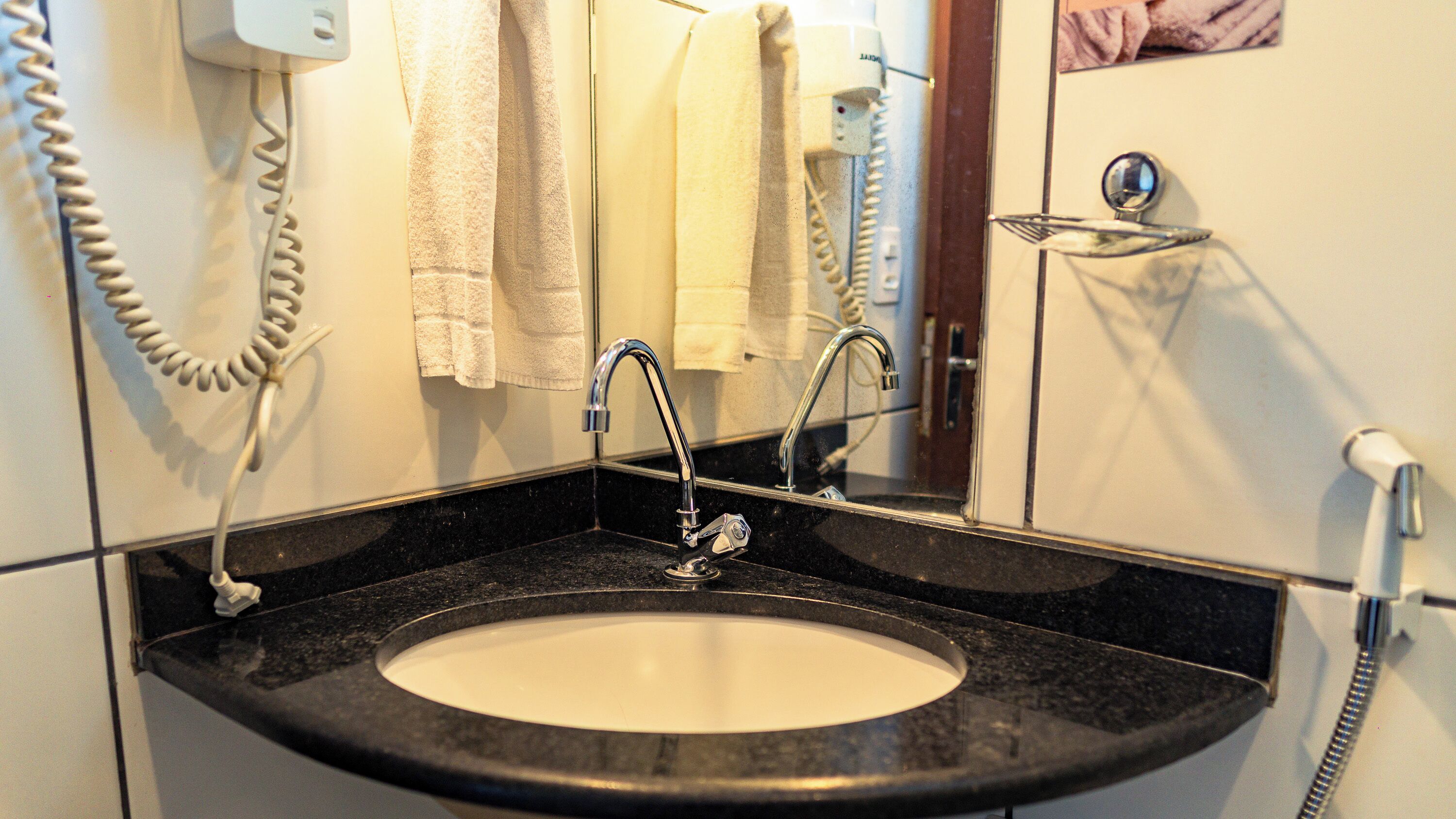A bathroom with a black granite sink, two faucets, a mirror, and a towel rack.