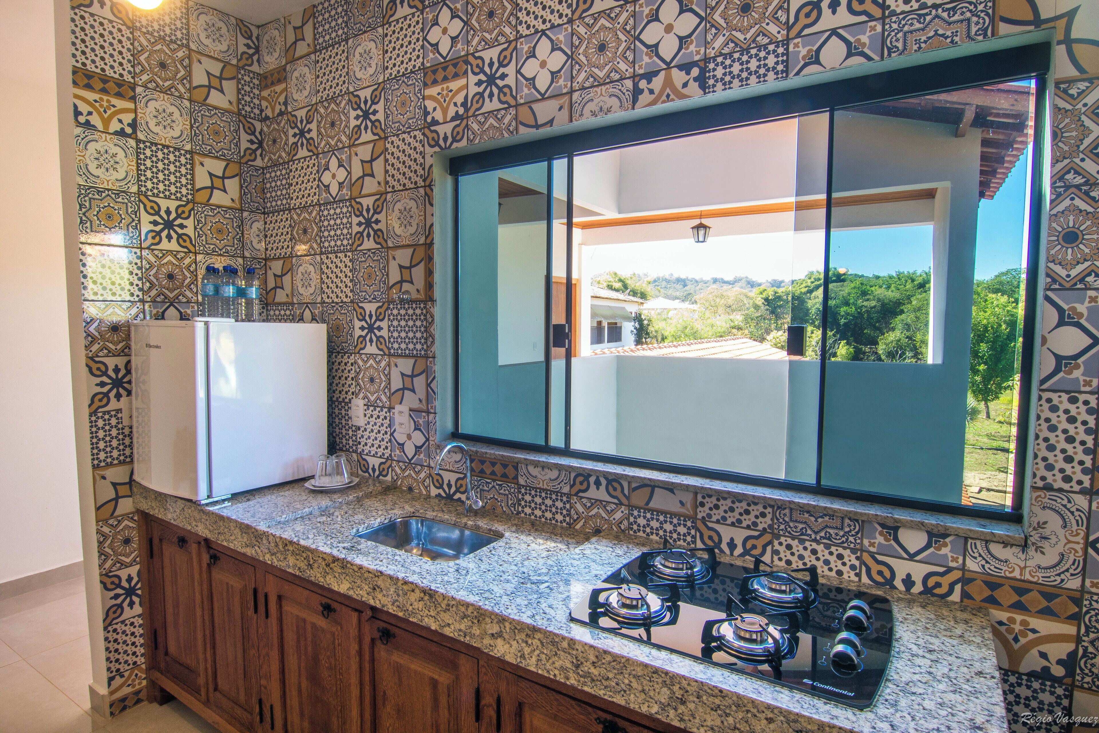 Cozinha com azulejos estampados, fogão embutido e uma grande janela com vista para o exterior.