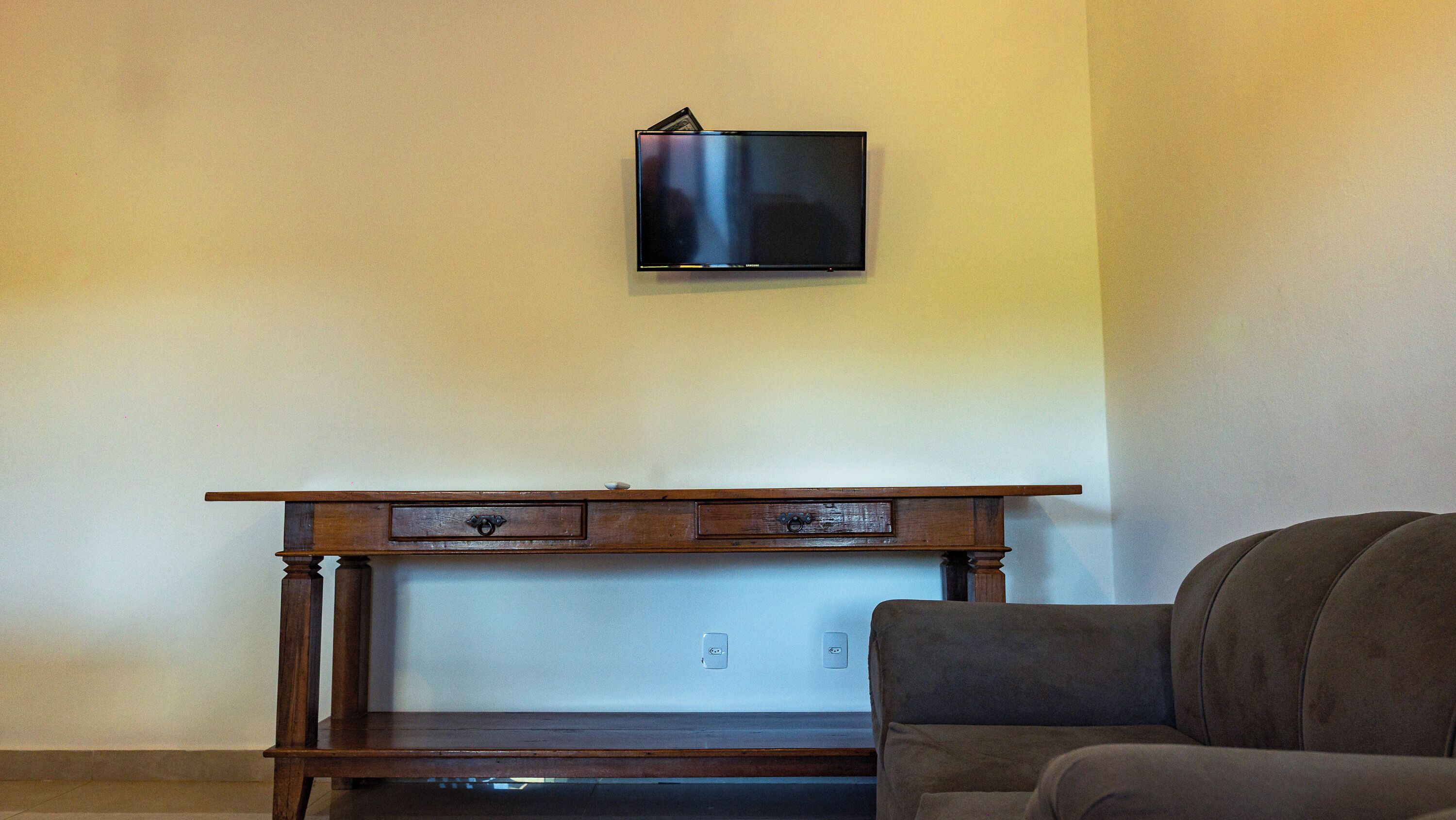 A room with a wooden console table, a flat-screen TV mounted on the wall, and a brown armchair.