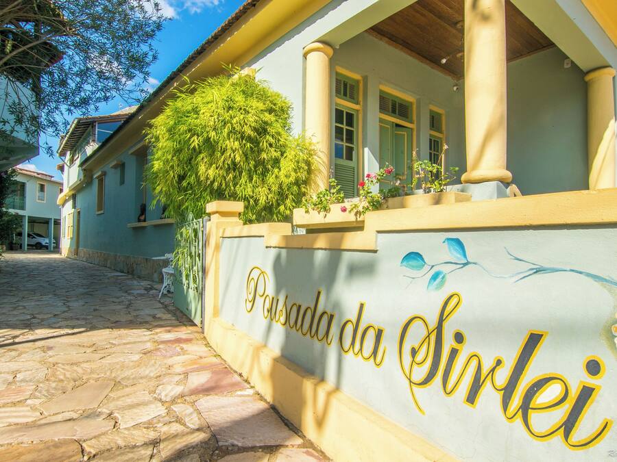 A building with a sign reading 'Pousada da Sirlei' and a stone-paved path leading to it.