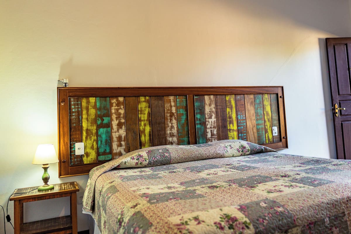 Ein Schlafzimmer mit einem hölzernen Kopfende, einer blumigen Bettdecke, einer Nachttischlampe und einer Tür rechts.