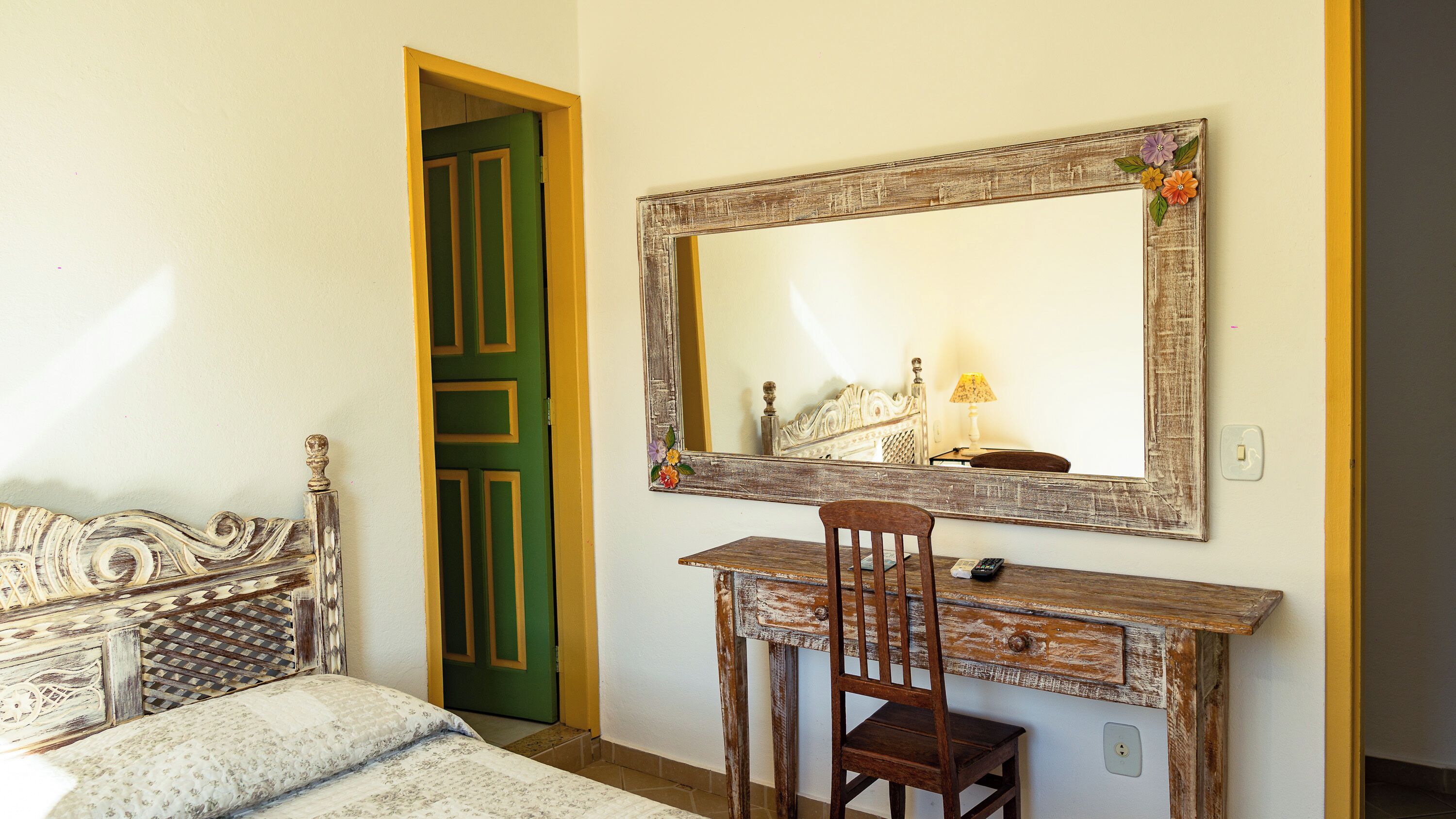 Quarto com uma cama, escrivaninha de madeira, cadeira, espelho e porta verde.
