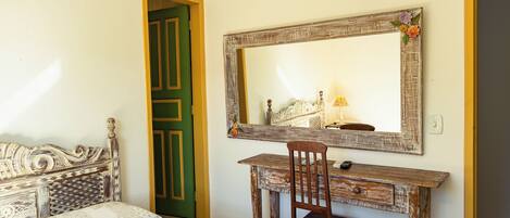 A bedroom with a bed, a wooden desk, a chair, a mirror, and a green door.