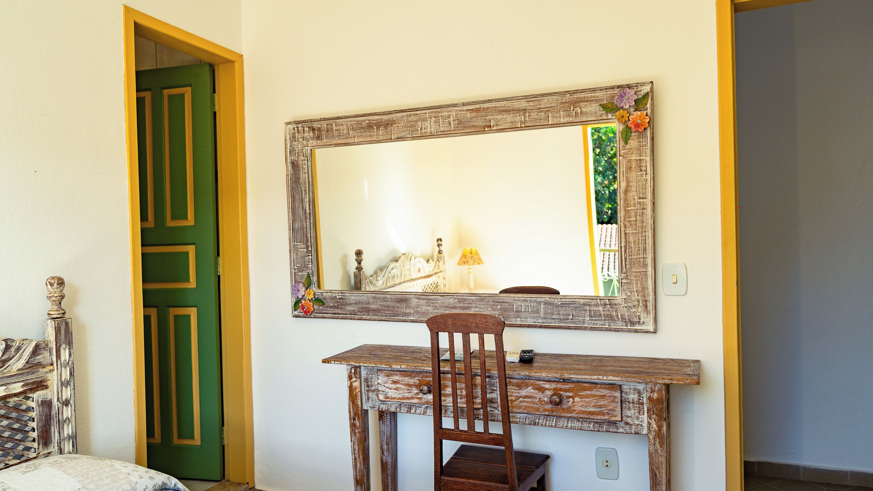 Una habitación con un escritorio de madera, una silla, una puerta verde y un espejo con adornos florales.