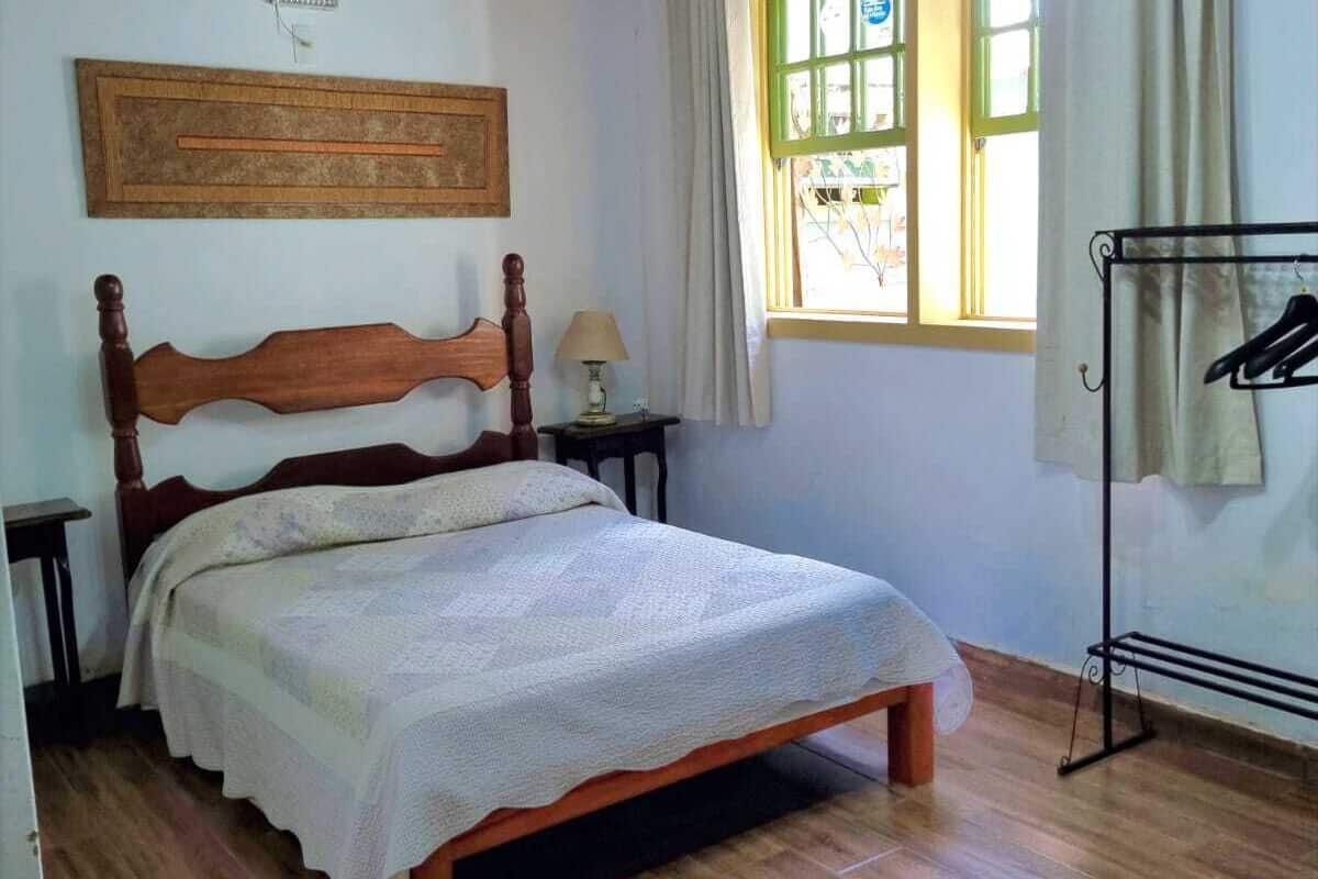 Ein Schlafzimmer mit einem hölzernen Bett, einem fenster mit Vorhängen, einer Wand-Klimaanlage und einem Holzboden.
