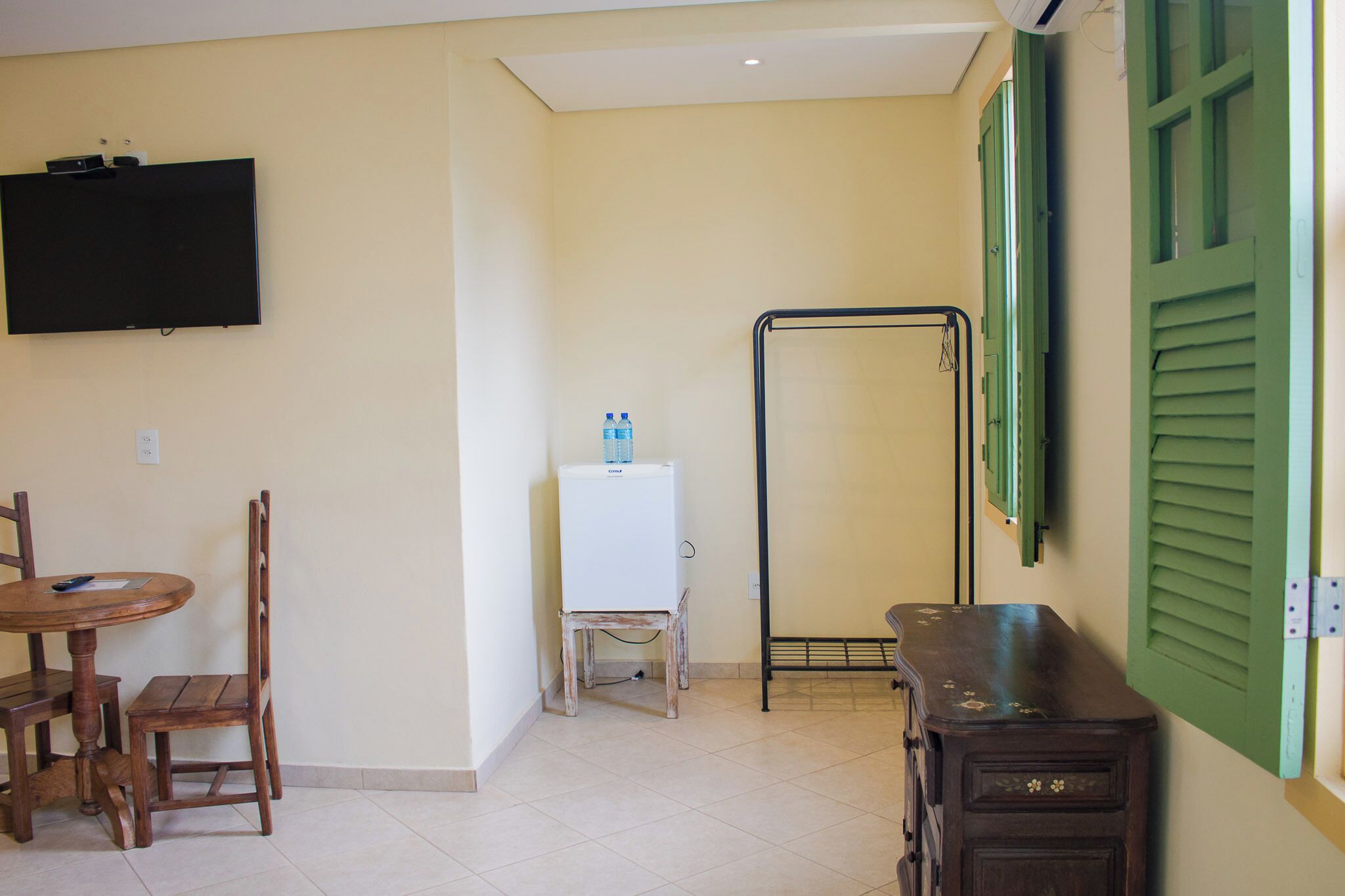 A room with a TV mounted on the wall, a small table with chairs, a water dispenser, and a cabinet.