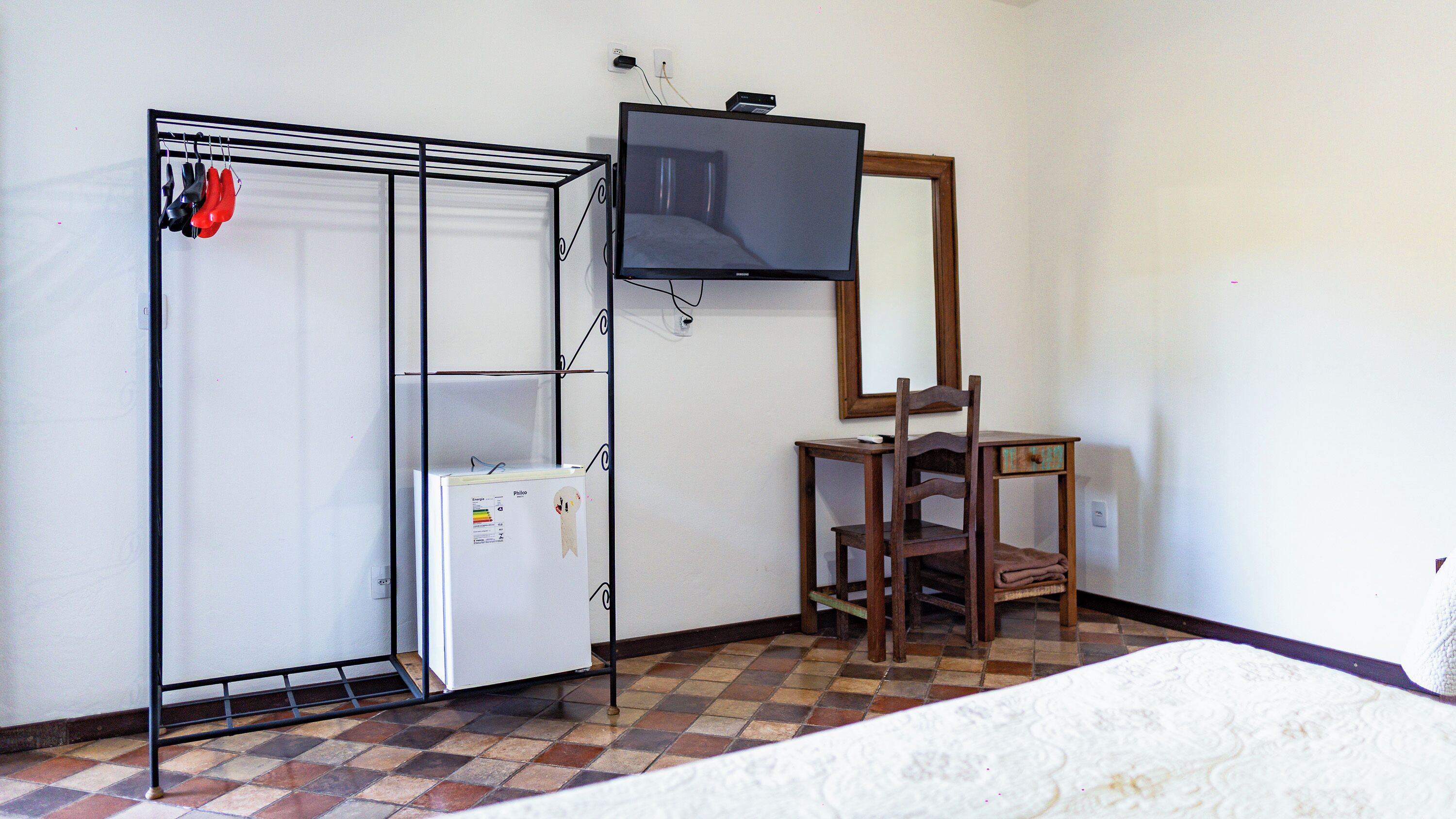 Habitació amb un llit, televisió penjada a la paret, una cadira de fusta i un armari amb mirall.