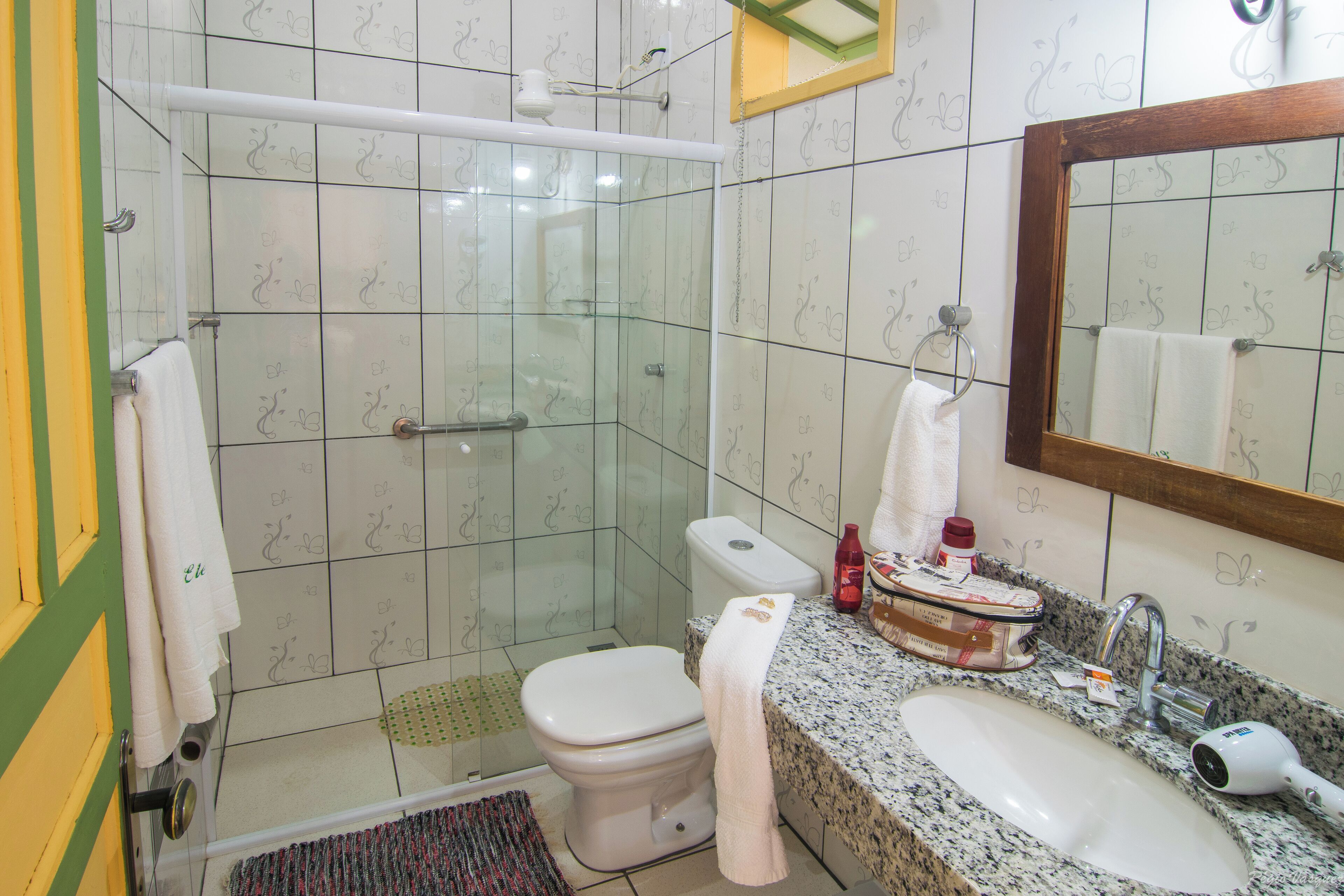 A bathroom with a glass-enclosed shower, a toilet, a sink with a mirror, and a towel rack.
