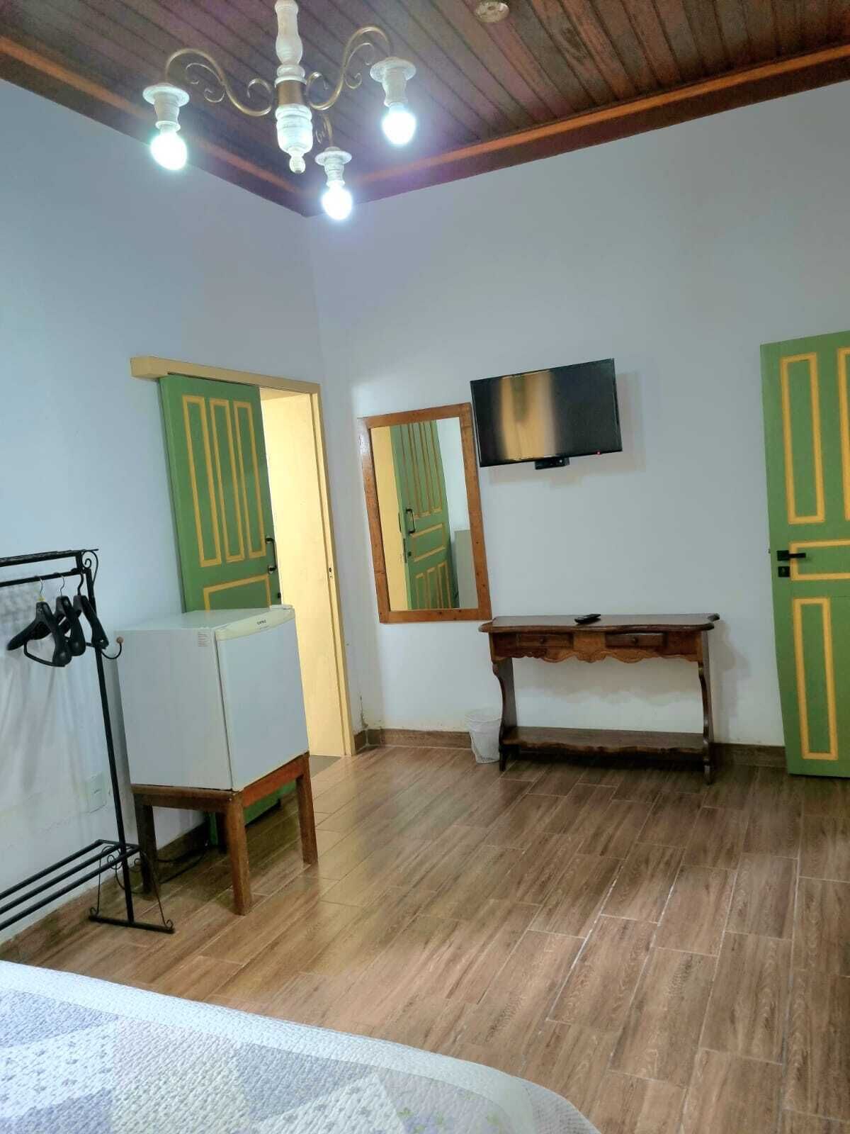 Une pièce avec un plafond en bois, un lustre, un téléviseur fixé au mur, une table en bois et des portes vertes.