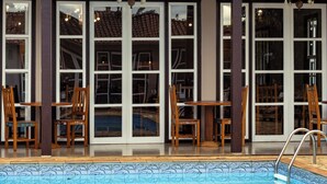 A swimming pool with a tiled deck, wooden chairs, and a building with large windows and a tiled roof. - Pousada da Sirlei (Tiradentes)
