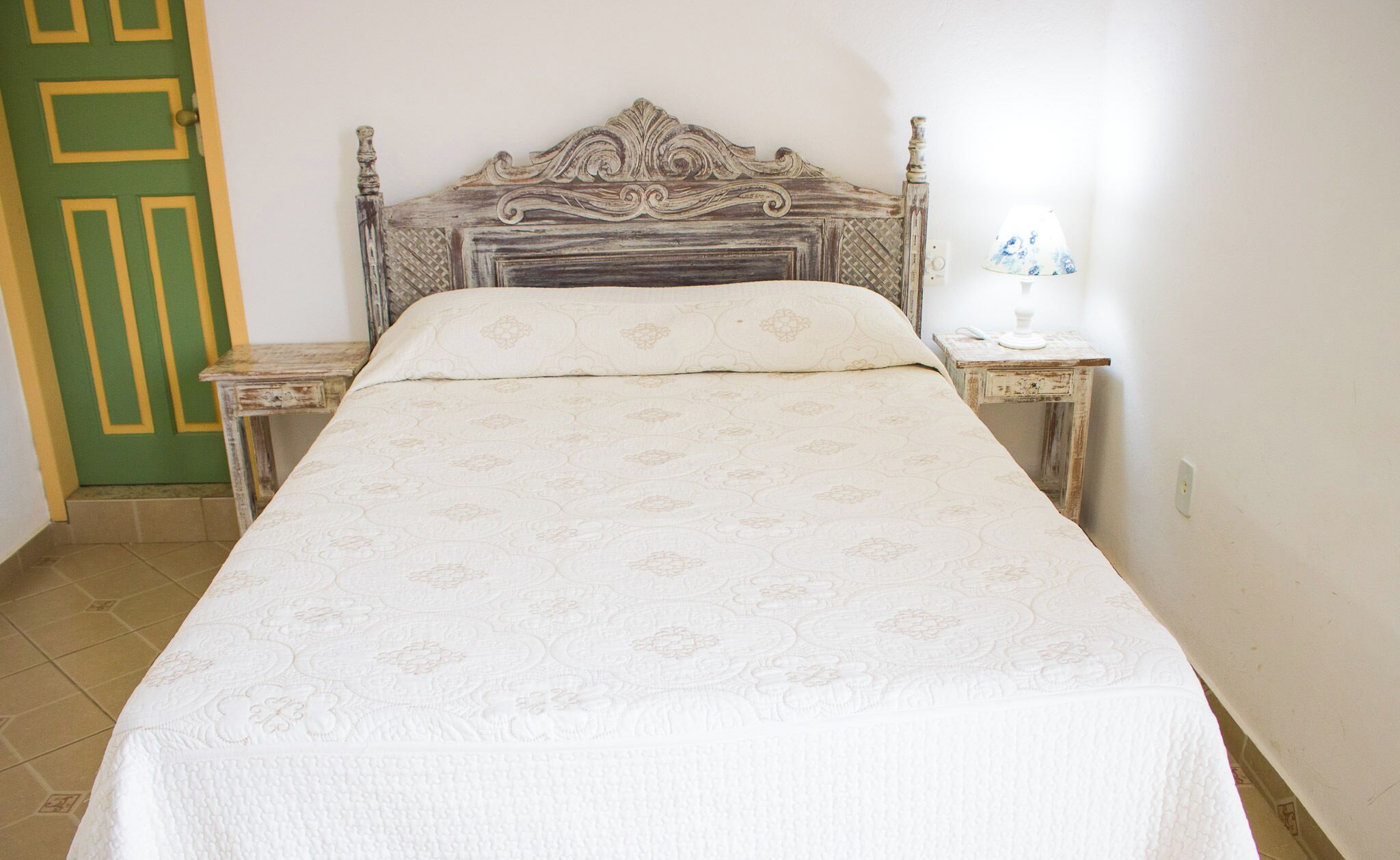 Una cama con colcha estampada, un cabecero de madera y dos mesitas de noche con lámparas.