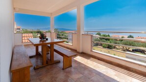 A balcony with a wooden table and a bowl of fruit, overlooking a coastal view with buildings and a clear sky. - Beautiful apartment in Jasenice with WiFi (Jasenice)