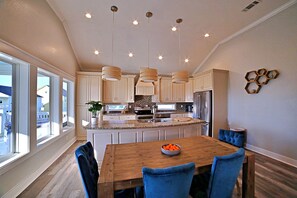 Une cuisine moderne avec une table à manger en bois, des chaises bleues et des luminaires suspendus.