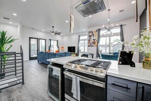 A modern kitchen with a central island, built-in oven, and a dining area with a blue sofa. - Cozy Spring View - Minutes to Energy Corridor, Galleria, Downtown & NRG Stadium (Houston)