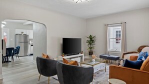 Una sala de estar moderna con un televisor de pantalla plana, sofás oscuros, una mesa de centro y un ventanal con cortinas.