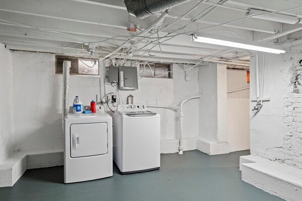 A laundry room with two washing machines, a dryer, and a utility room with exposed pipes and electrical wiring. - Newly-renovated 2-bedroom House with a Luxurious Massage Chair (Springfield)