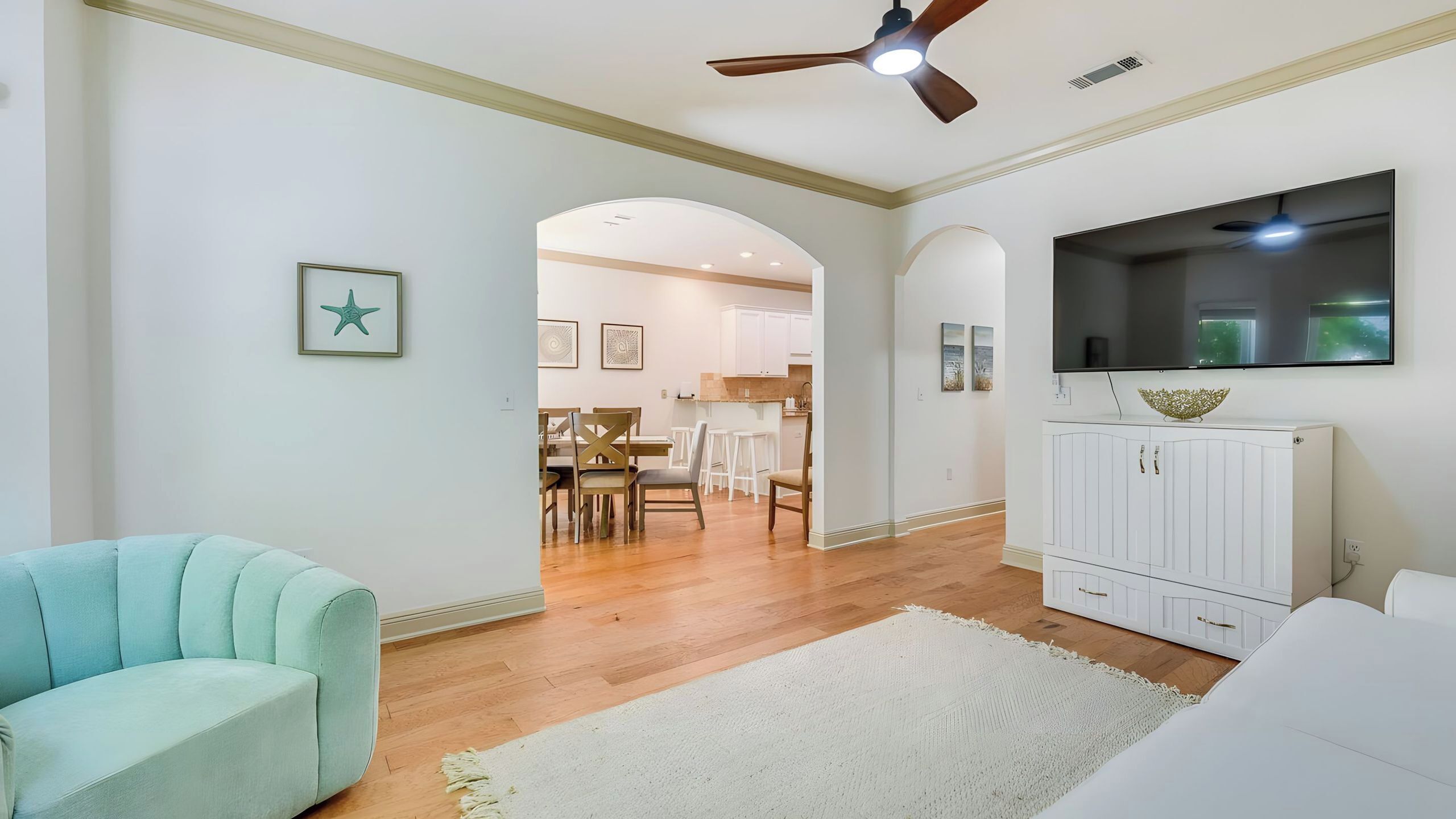 A living room with a ceiling fan, a TV, and a dining area with chairs and a table.