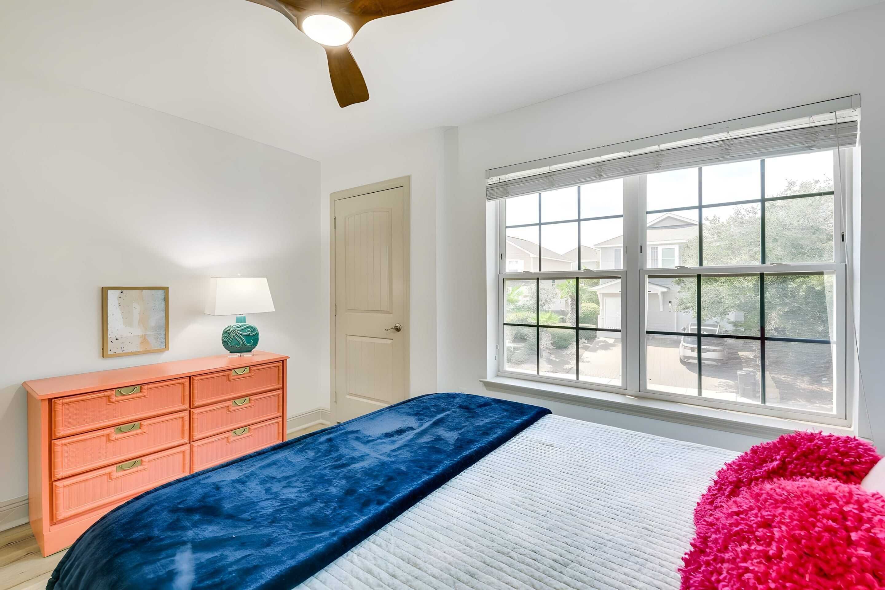 Une chambre à coucher avec un lit, une commode, une fenêtre et un ventilateur de plafond.