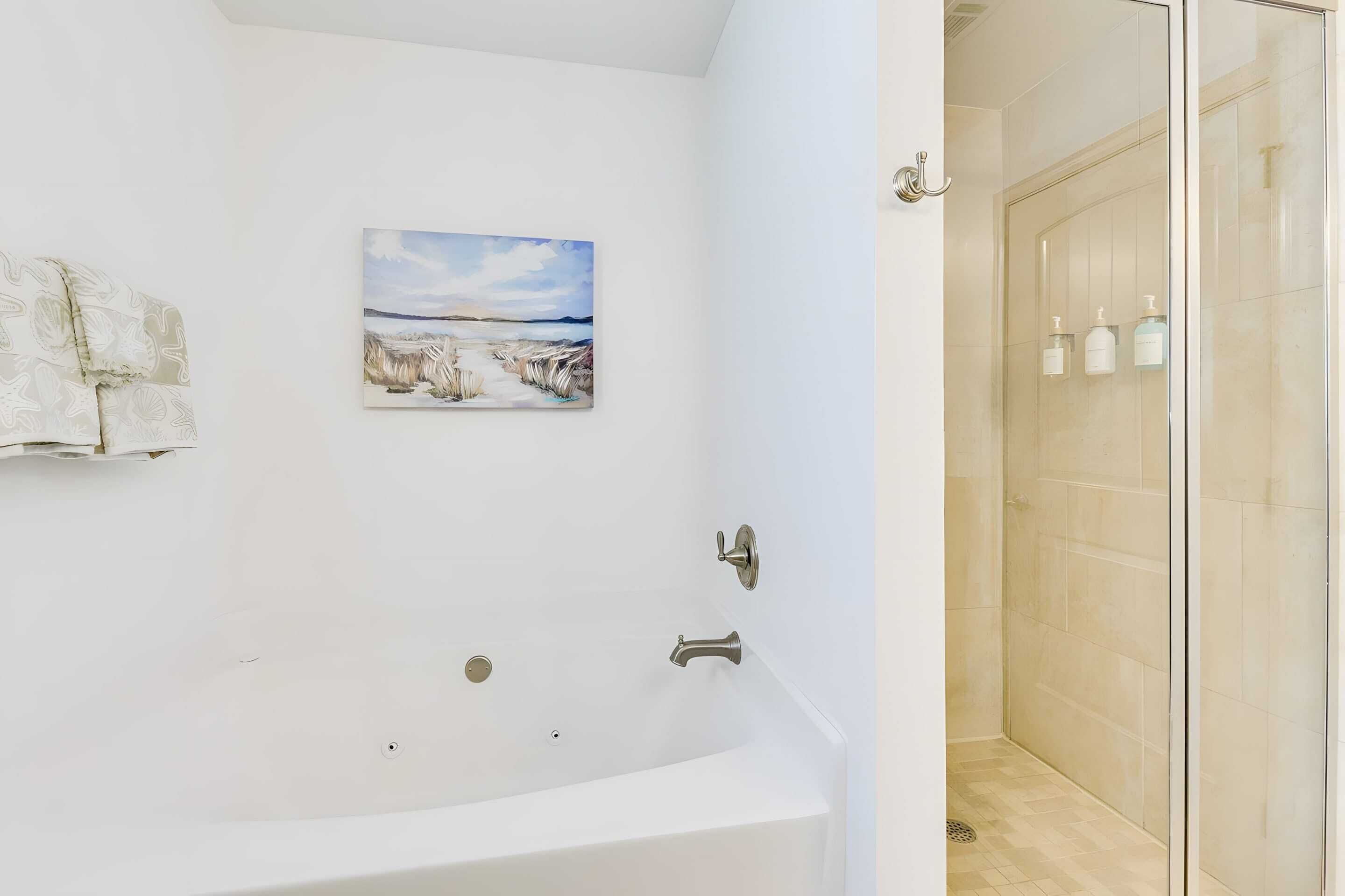 Un baño con una bañera blanca, cabina de ducha de vidrio y un cuadro en la pared.