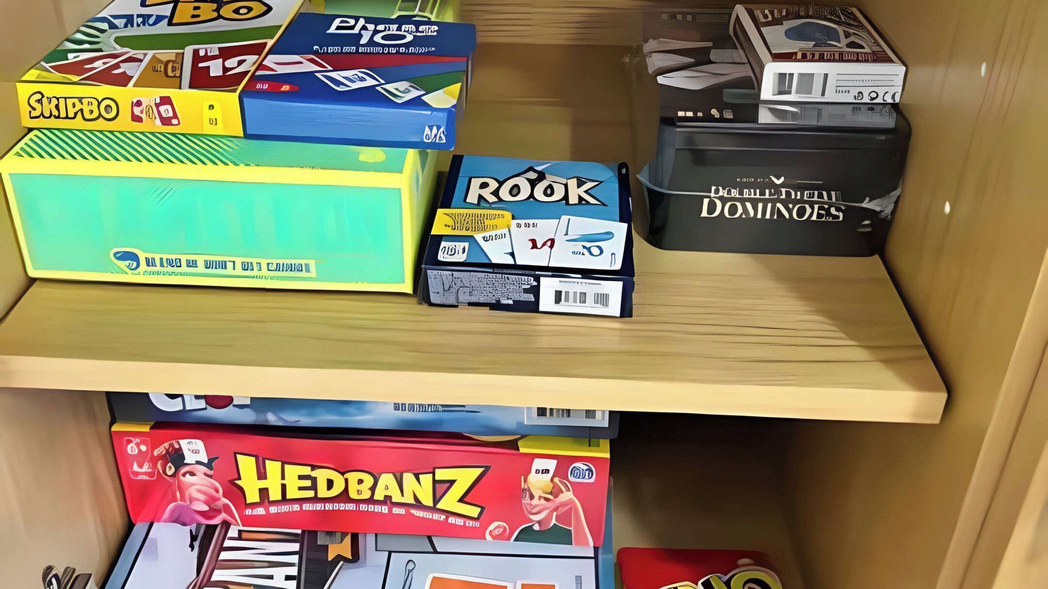A shelf with various board game boxes, including Skipbo, Photo, Rook, and Hedbanz.