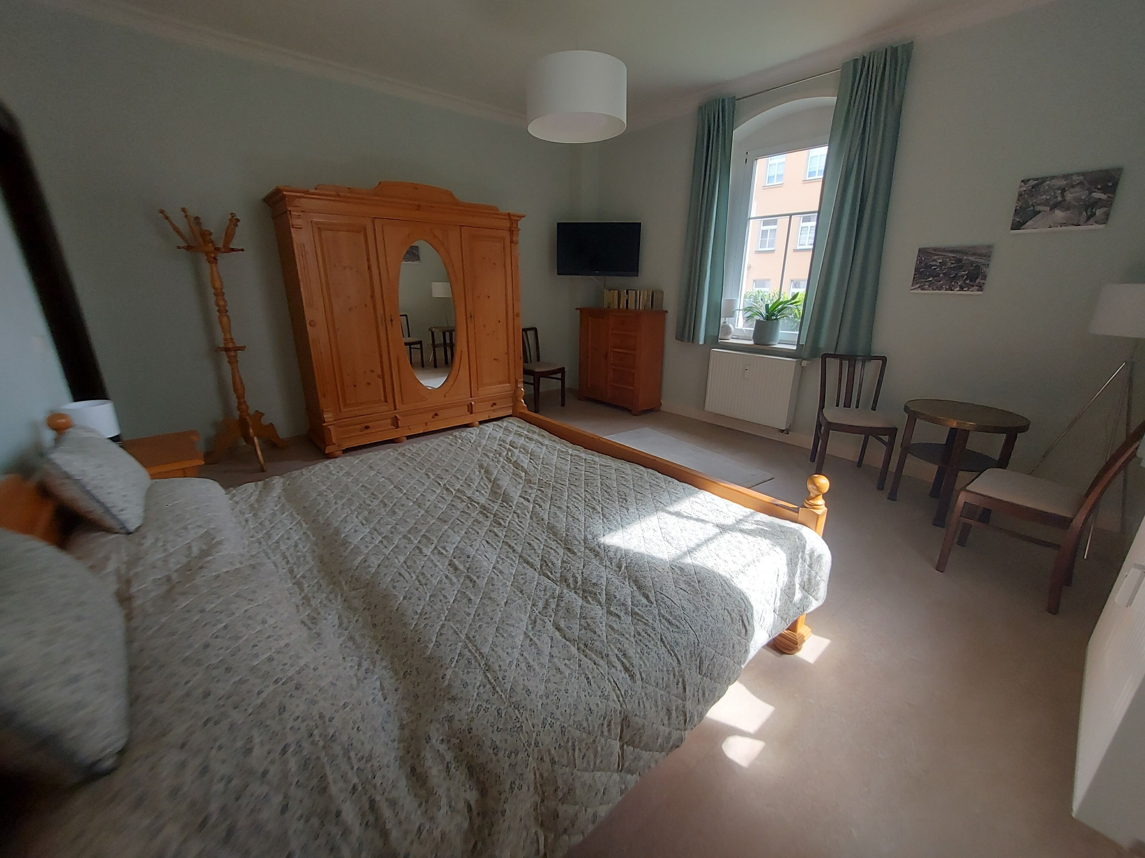 Ein Schlafzimmer mit einem großen Bett, einem Holzschrank, einem Fernseher, einem Fenster mit Vorhängen und einem kleinen Tisch mit Stühlen.