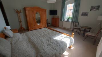 Ein Schlafzimmer mit einem großen Bett, einem Holzschrank, einem Fernseher, einem Fenster mit Vorhängen und einem kleinen Tisch mit Stühlen.