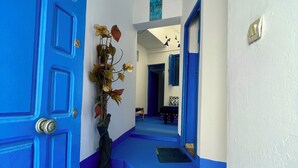 A hallway with blue-painted walls and doors, leading to a room with a bed and a window. - Don't miss this unique blue planet. (Asilah)