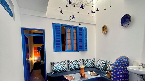 A room with a blue carpet, a sofa with patterned cushions, a coffee table, and a skylight with hanging decorations. - Don't miss this unique blue planet. (Asilah)