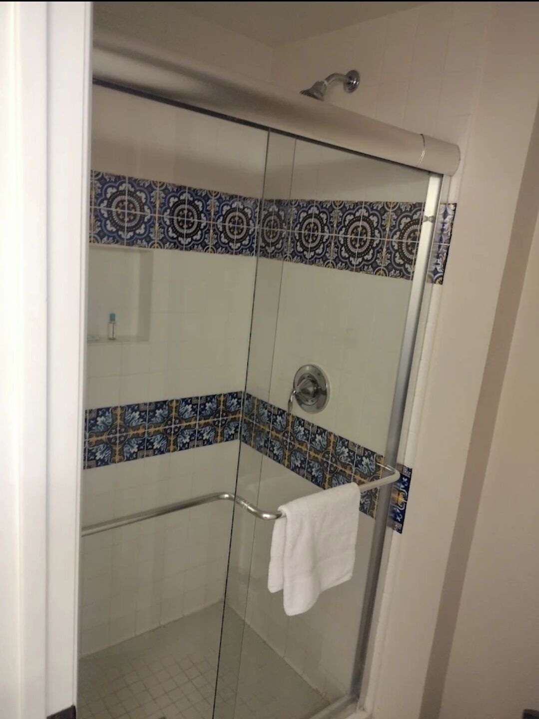 A glass-enclosed shower with a white towel on a rack, patterned tiles on the walls, and a showerhead above.