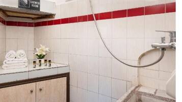 A shower room with a tiled wall, a shower head, a towel rack with towels, and a small plant.