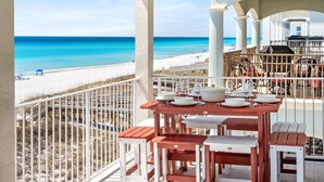 Balcón con mesa lista para comer, con vista a una playa de aguas azules y arena.