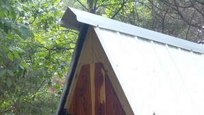 Eine Holzhütte mit geneigtem Dach, umgeben von natürlicher Vegetation.