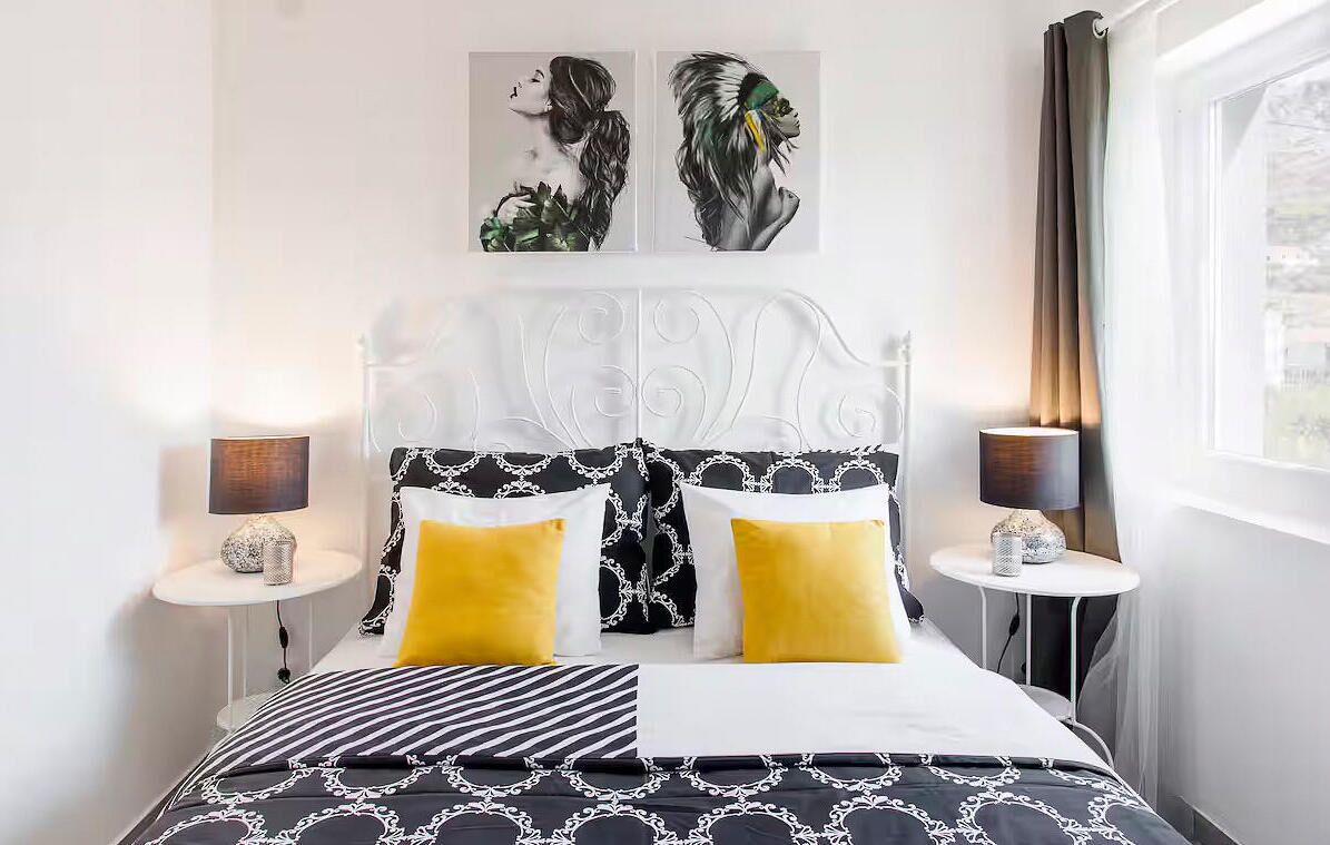 Ein modernes Schlafzimmer mit einem schwarz-weißen Bettbezug, zwei gelben Kissen und einem dekorativen Kopfteil.