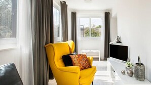 A modern living room with a yellow armchair, a flat-screen TV, and a white console table with decorative items. - Gorgeous home in Mravince (Mravince)