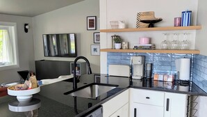 A modern kitchen with a black countertop, white cabinets, and a built-in dishwasher. There are shelves above the sink holding various kitchen items and a few framed pictures on the wall. - Charming 3-bedroom house with WiFi, fitness room in Pontiac (Pontiac)