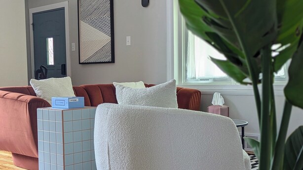 A living room with a sofa, a white pouf, a tiled side table, and a potted plant. - Charming 3-bedroom house with WiFi, fitness room in Pontiac (Pontiac)