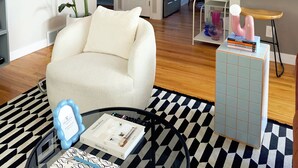 A modern living room with a white armchair, a black and white patterned rug, and a coffee table with a book and a decorative item. - Charming 3-bedroom house with WiFi, fitness room in Pontiac (Pontiac)