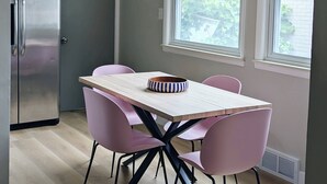 A modern kitchen with a stainless steel refrigerator, a wooden table with pink chairs, and a hanging light fixture. - Charming 3-bedroom house with WiFi, fitness room in Pontiac (Pontiac)