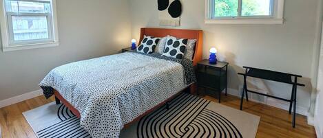 A bedroom with a bed, a ceiling fan, two bedside tables with lamps, a bench, and two windows.