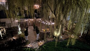 A nighttime garden with a stone pathway, decorative urns, and string lights.