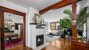 A spacious living room with a fireplace, a dining area with a red rug, and a piano.
